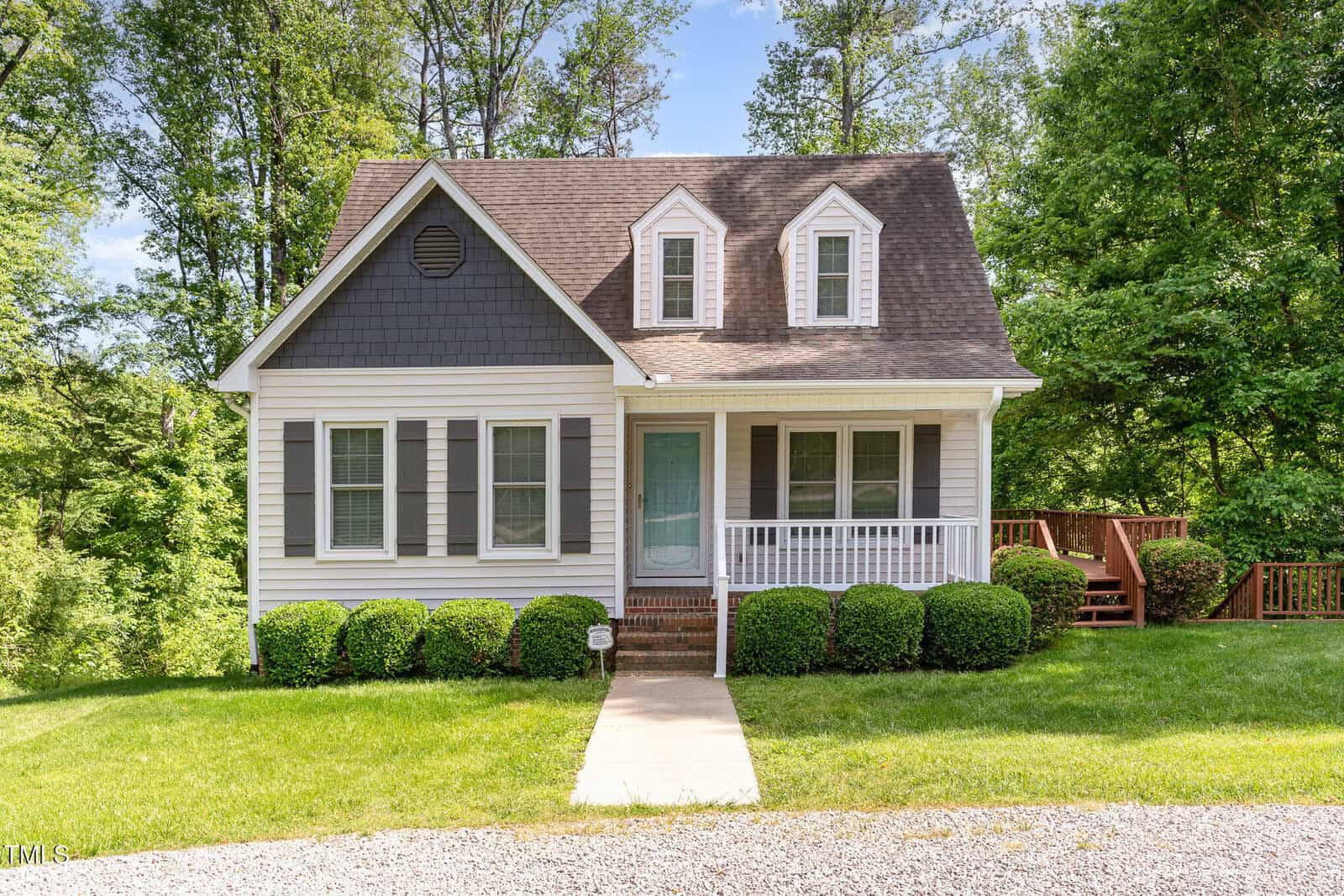 A small two-story house at 200 Weybossett Road in Henderson with gray siding, white trim, and a covered front porch. Three front windows, a blue door, and steps to a wooden deck on the right are surrounded by green grass and trees.