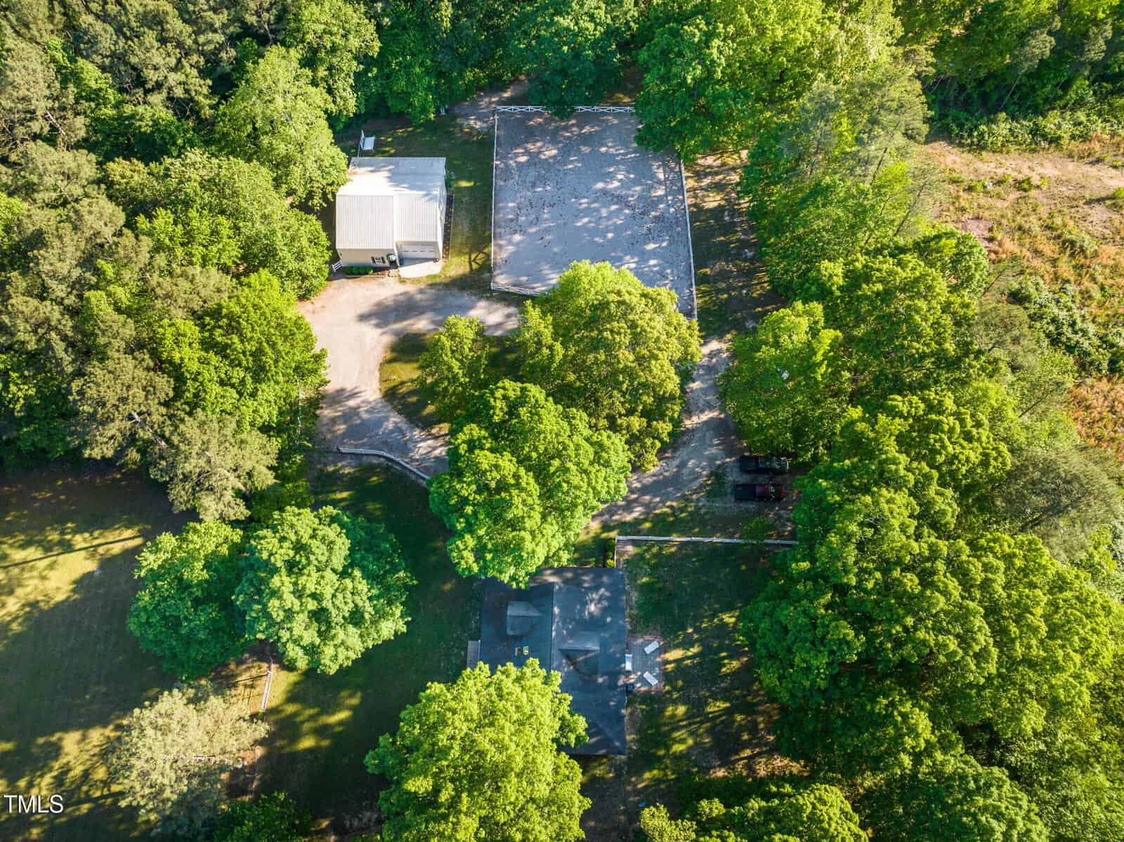 Aerial view of a property with three buildings surrounded by trees. The buildings are spaced apart, with driveways and open areas visible between them, and dense greenery covers much of the surrounding land.