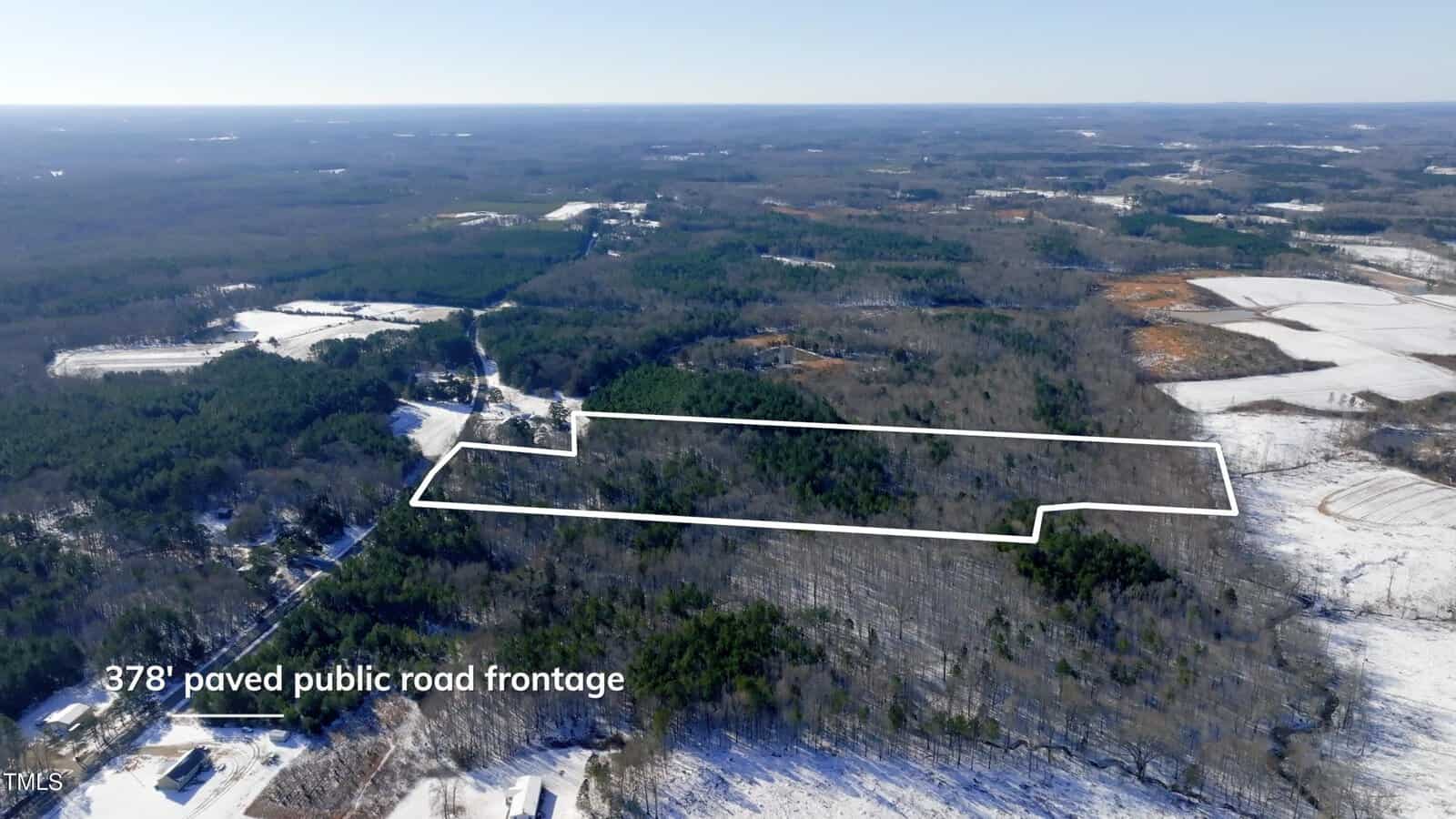 Aerial view of a rectangular, forested plot of land outlined in white, surrounded by snow-covered areas and trees. Text indicates "378' paved public road frontage" along the bottom edge of the property.