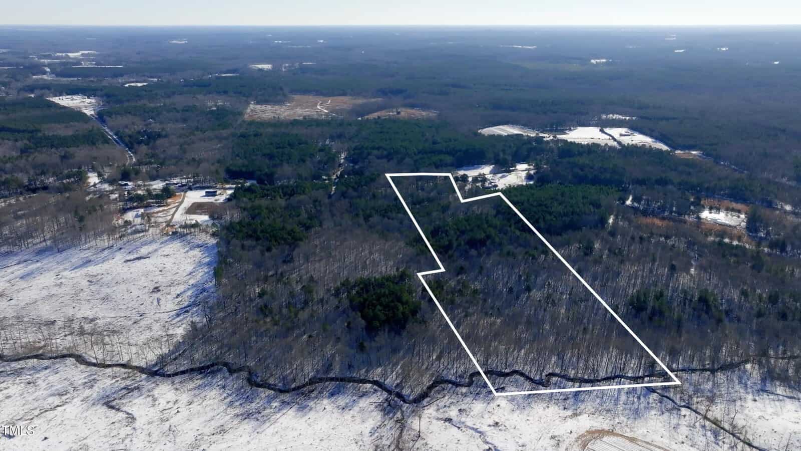 Aerial view of a snow-covered rural landscape with a rectangular wooded area outlined in white, showing property boundaries among surrounding forest and open fields.