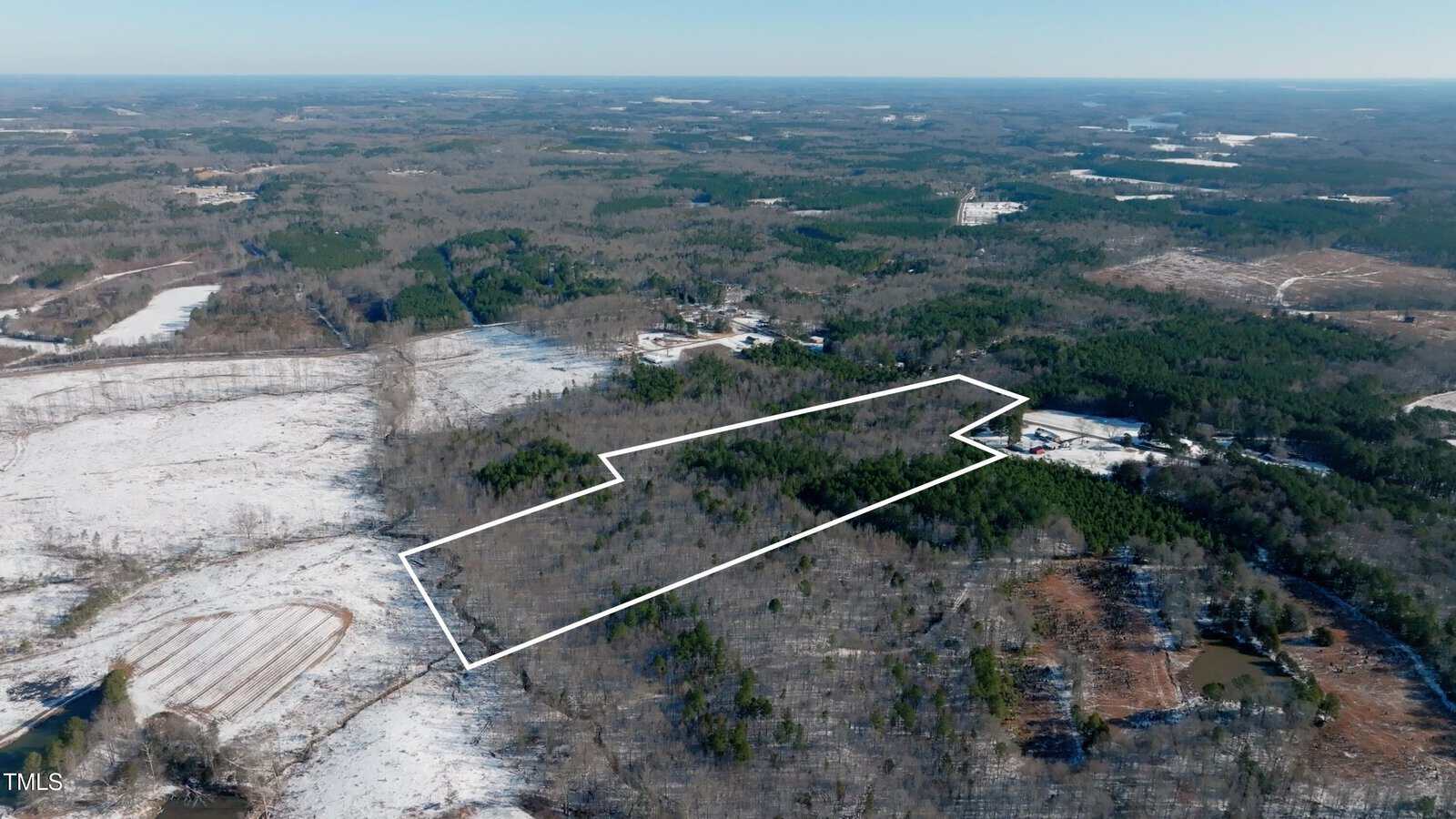 Aerial view of a large, wooded, and partially snow-covered rural landscape with a white outline marking the boundary of a specific property area. Surrounding areas include trees, fields, and scattered buildings.