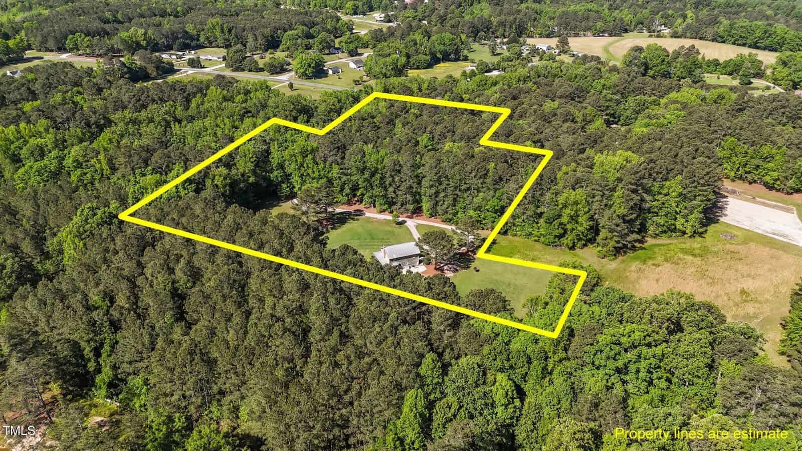 Aerial view of a large wooded property with a house, outlined in yellow to show estimated property lines. Surrounding area includes dense trees, open fields, and scattered homes.