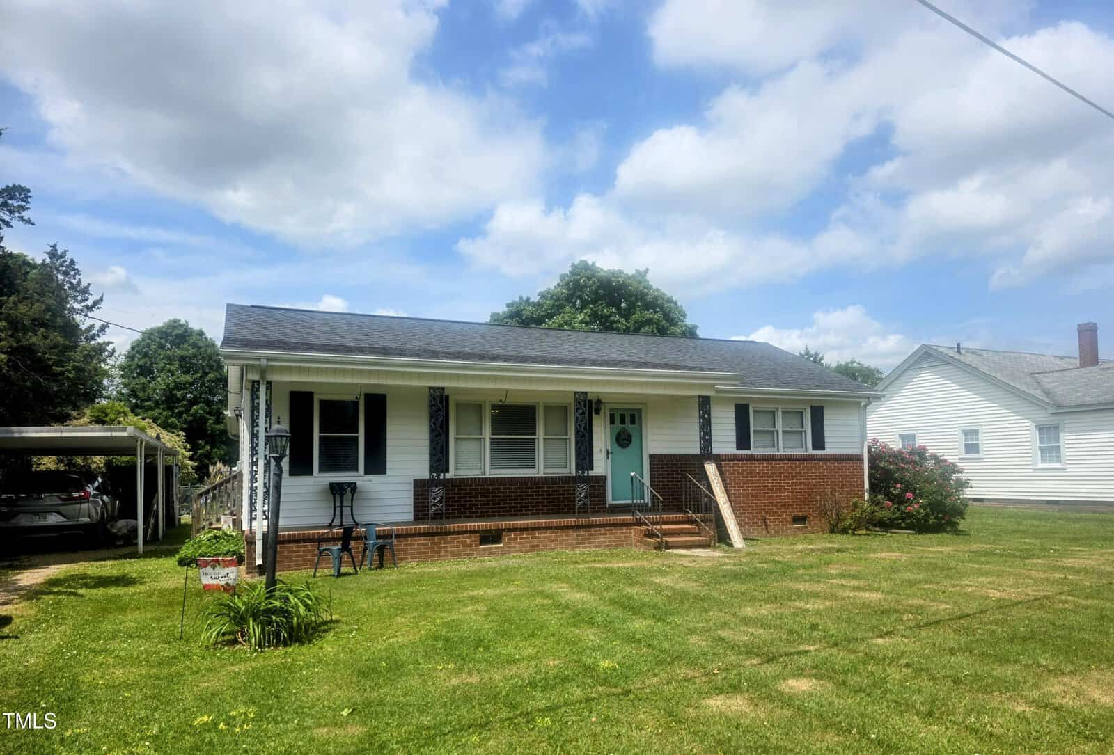 Charming single-story brick house at 66 Epsom Rocky Ford Road, Henderson, with white siding, black shutters, and a front porch with decorative columns. Enjoy a grassy yard, small garden by the porch, carport, and neighboring homes on each side.