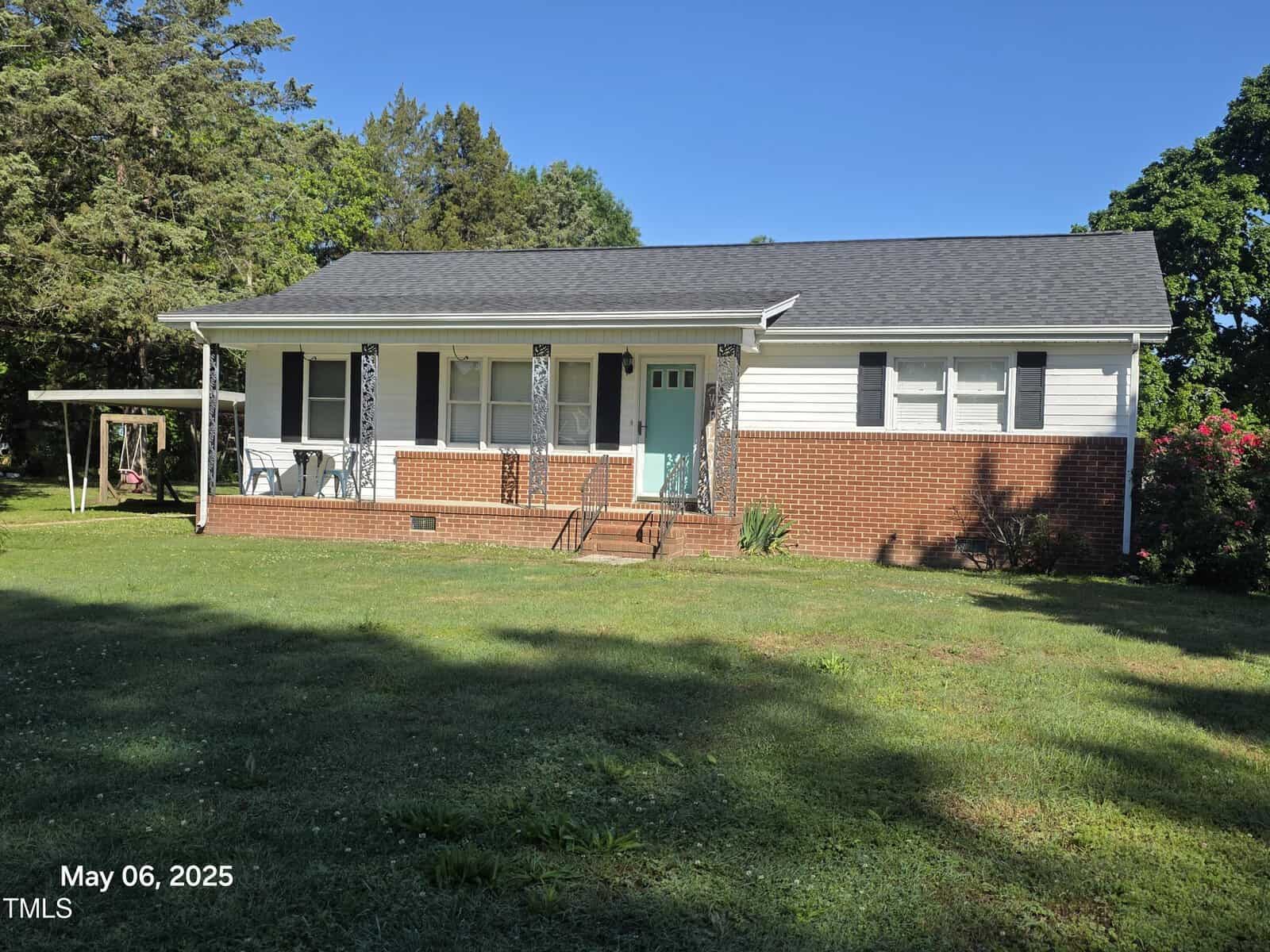 Charming single-story home in Henderson at 66 Epsom Rocky Ford Road, featuring a brick lower exterior with white siding, black shutters, a teal front door, covered porch with decorative metal columns, and a large grassy yard under a clear blue sky.