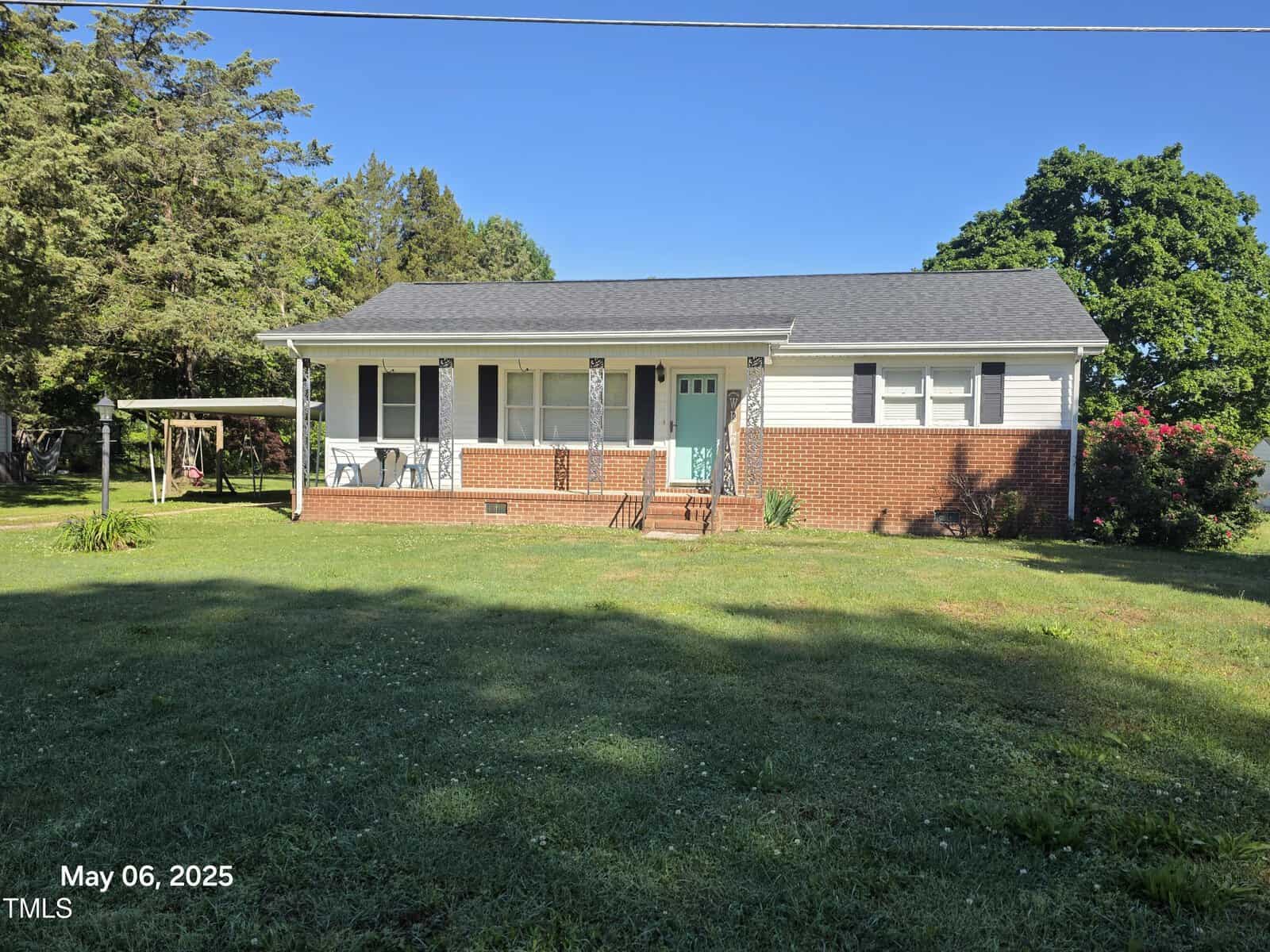 A single-story house at 66 Epsom Rocky Ford Road, Henderson, with white siding and red brick, a porch with decorative posts, a turquoise front door, and a swing set in the yard. Trees and grass surround the home. The date reads May 06, 2025.