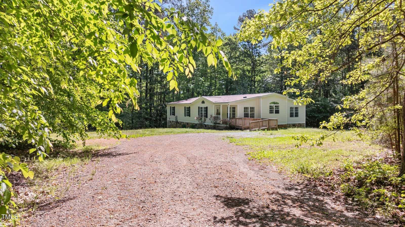 A single-story manufactured home with a small front porch sits at the end of a gravel driveway on 2690 Rivers Edge Road in Oxford, surrounded by trees and greenery on a sunny day.