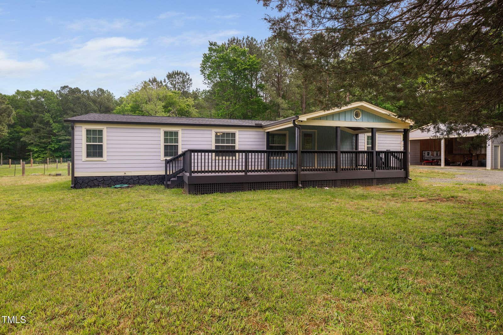 Charming single-story manufactured home at 2680 Olmstead Road in Creedmoor, featuring light gray siding, a covered front porch with wooden ramp and railing, surrounded by grass and trees, next to a gravel driveway and shed.