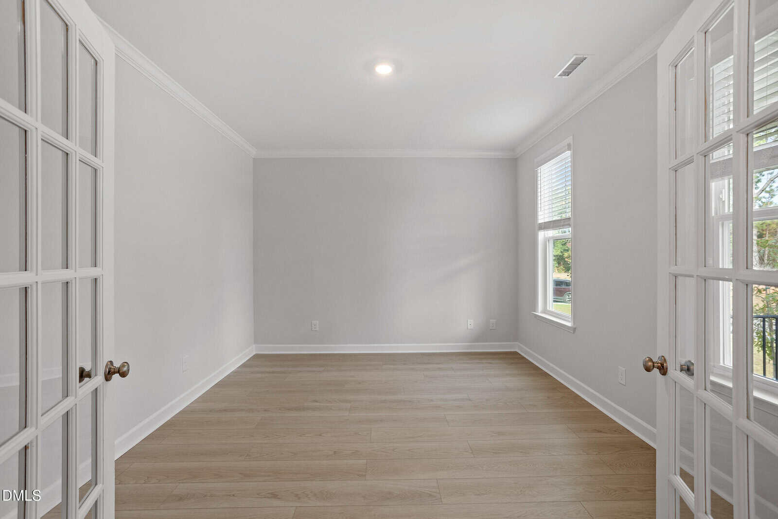 A bright, empty room with light wood floors, light gray walls, and white trim. The room has two sets of French doors and several windows letting in natural light.