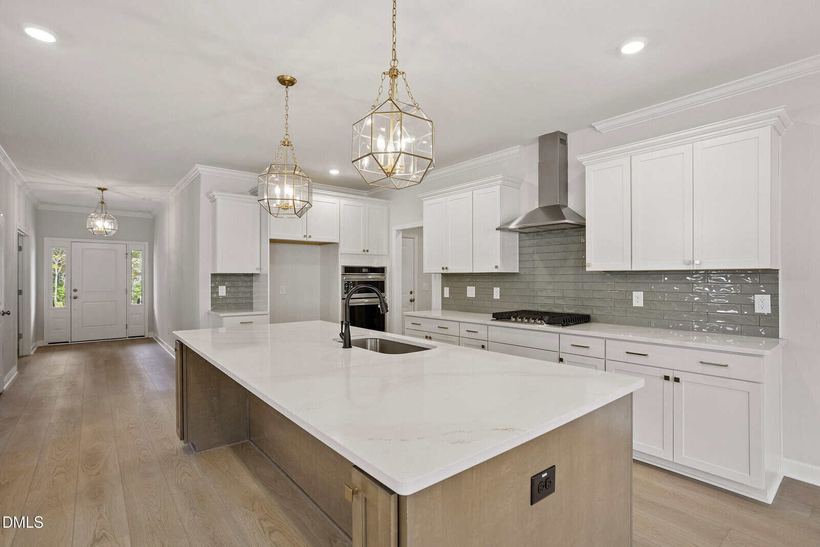 Modern kitchen with white cabinets, a large island with a white countertop, pendant lights, stainless steel appliances, a gas cooktop, and a tile backsplash. Light wood floors and recessed lighting complete the space.