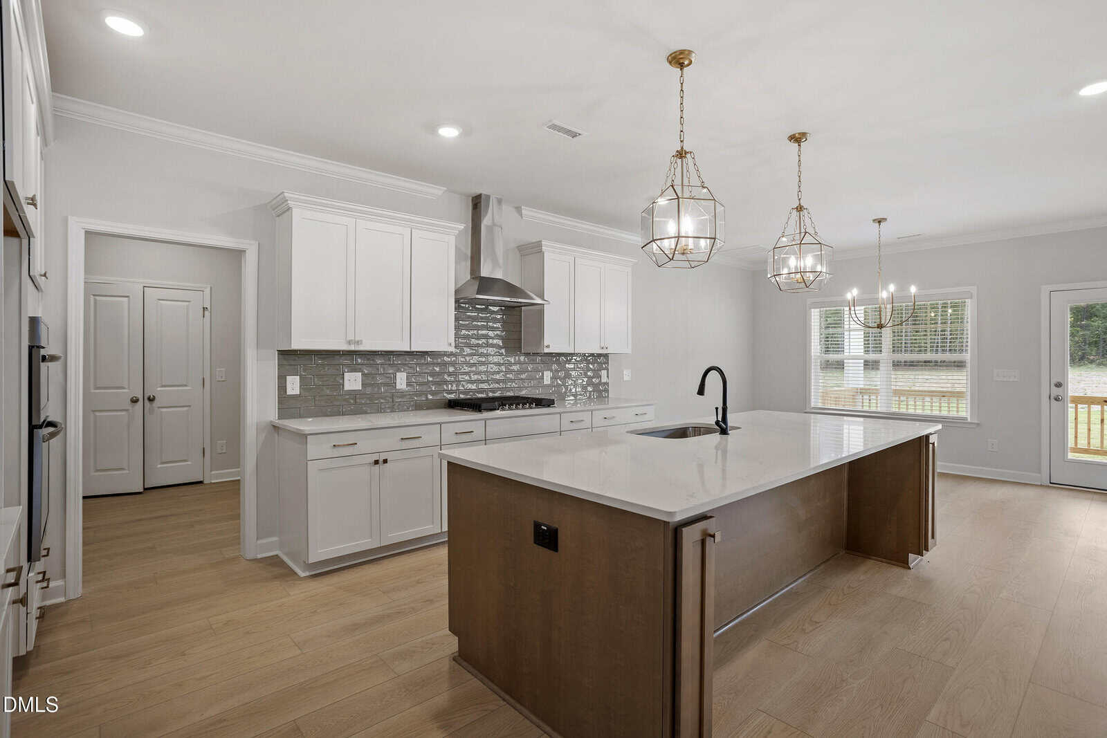 Modern kitchen with a large island, white cabinets, stainless steel appliances, subway tile backsplash, pendant lights, light wood floors, and large windows letting in natural light.