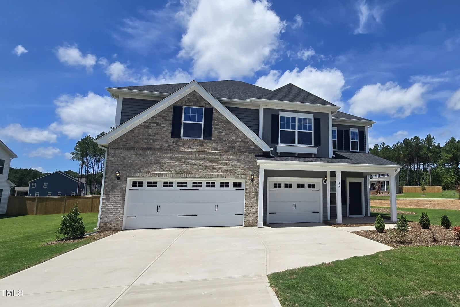 Two-story suburban house at 40 Accord Drive in Youngsville, featuring a brick and gray siding exterior, three-car garage, white trim, and dark blue shutters. Concrete driveway and landscaped front yard under a blue sky with scattered clouds.