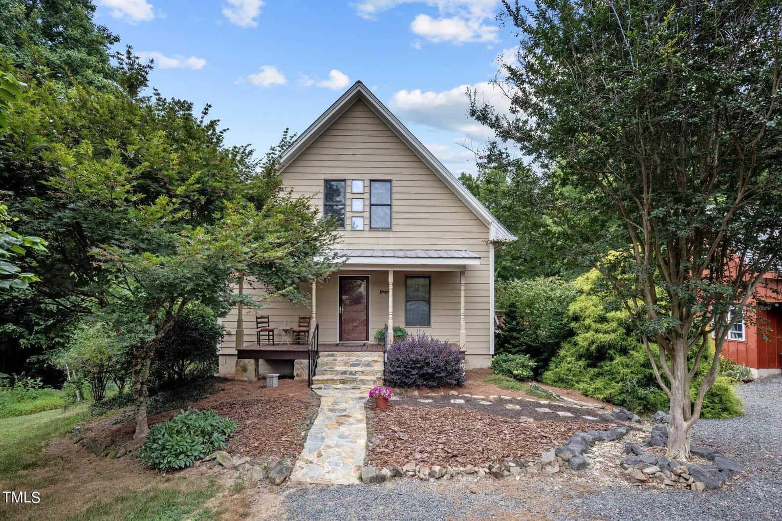 A beige two-story house at 260 Woody Lane, Oxford, features a front porch, steps leading up from a stone path, and is surrounded by trees and shrubs, with a gravel driveway in the foreground.