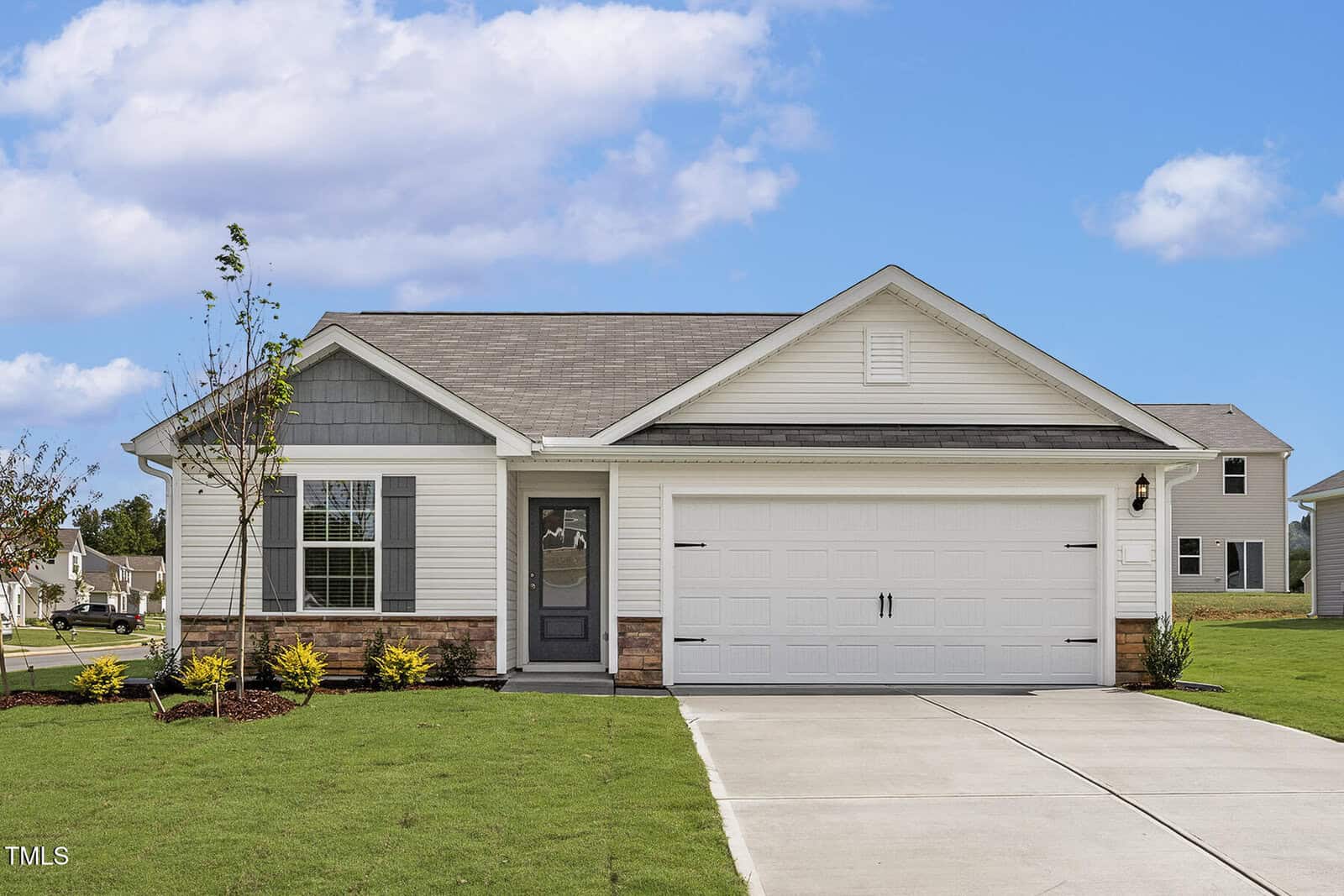 Charming single-story suburban house at 203 Benton Drive, Oxford, with white siding, gray shingles, and a double garage. The front lawn features small shrubs and a young tree by the driveway. Blue sky with scattered clouds in the background.