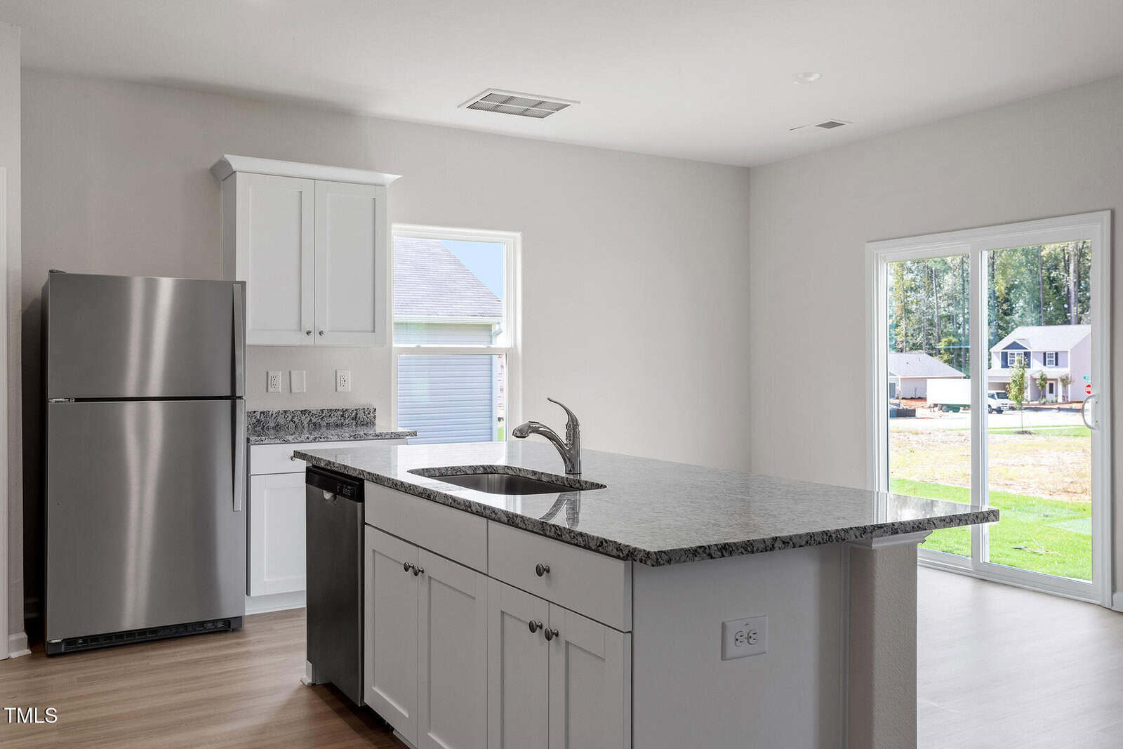 Modern kitchen with white cabinets, stainless steel refrigerator, granite countertops, and a center island with a sink. Large sliding glass doors provide access to the outdoors and allow natural light into the space.