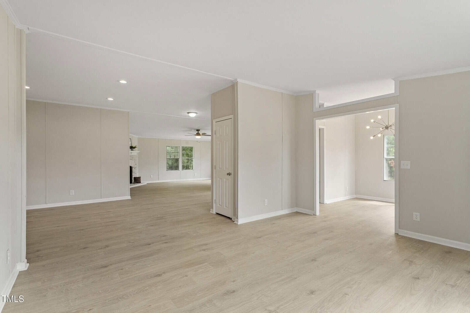 Spacious open-concept interior with light wood floors, neutral-colored walls, and recessed lighting. Multiple doorways and windows bring in natural light. A modern light fixture hangs in the adjacent room.
