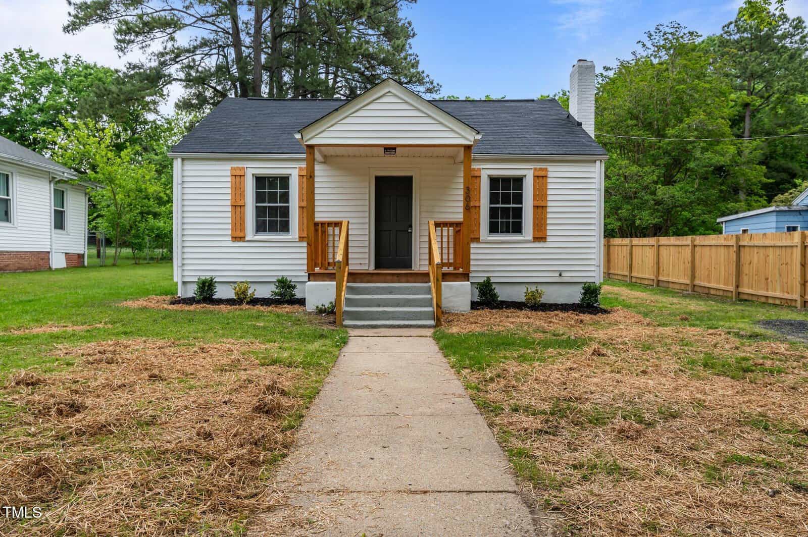 A small white single-story house at 306 Coleman Street, Oxford, with a gray shingled roof, wooden shutters, and a covered front porch. A concrete walkway leads to the steps and a fenced yard with trees in the background.