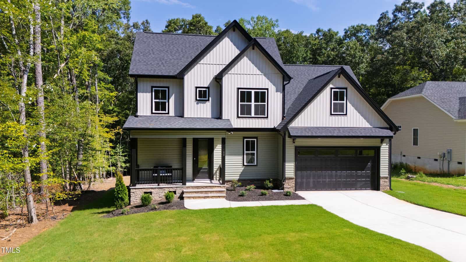 Two-story gray house with black trim, front porch, and attached two-car garage located at 188 Buckaroo Drive in Louisburg. The home is surrounded by green grass, landscaped shrubs, and trees in the background under a clear sky.
