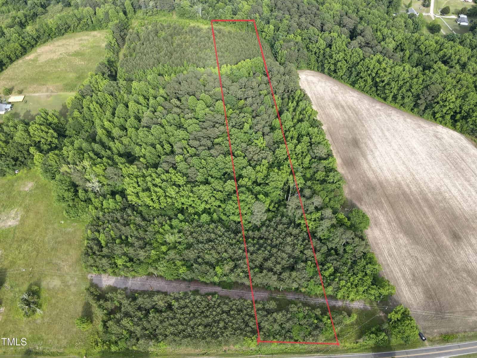 Aerial view of a rectangular wooded plot of land outlined in red, surrounded by other forested areas and a cultivated field, with a road running along the front edge.