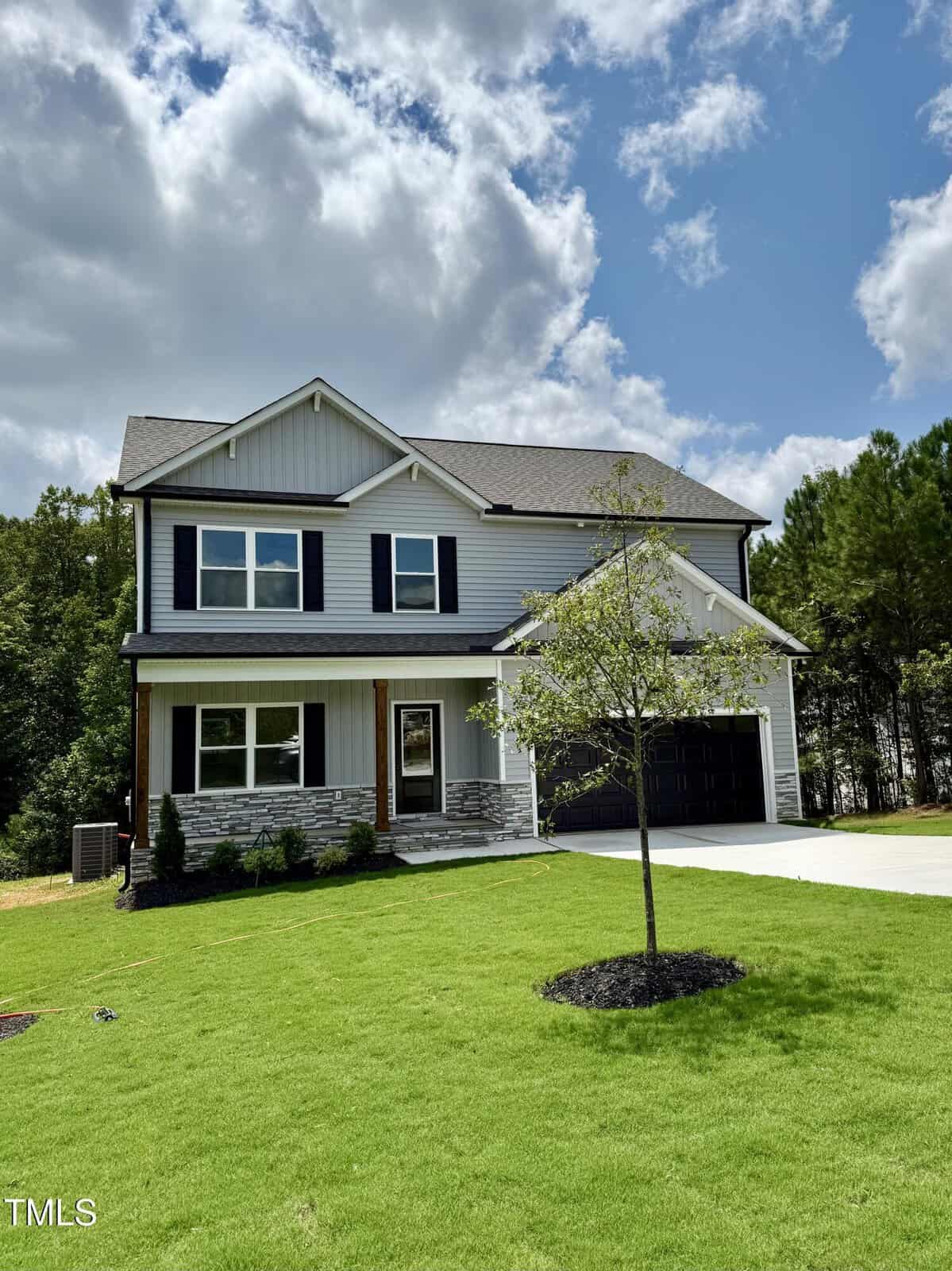 Two-story modern house at 50 Moonraker Drive with gray siding, black shutters, and a black garage door. The front lawn is neatly manicured, and a young tree stands in the yard under partly cloudy Spring Hope skies.