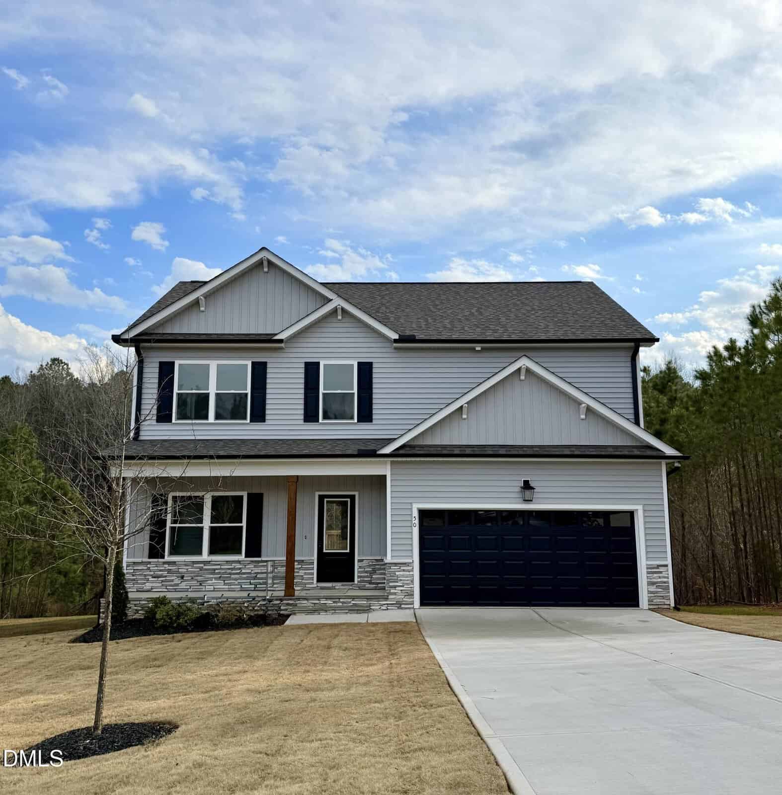 Two-story suburban house at 50 Moonraker Drive, Spring Hope, featuring gray siding, blue shutters, a blue garage door, a small porch, and stone accents. The lawn is neatly trimmed, and there are trees and a blue sky with clouds in the background.