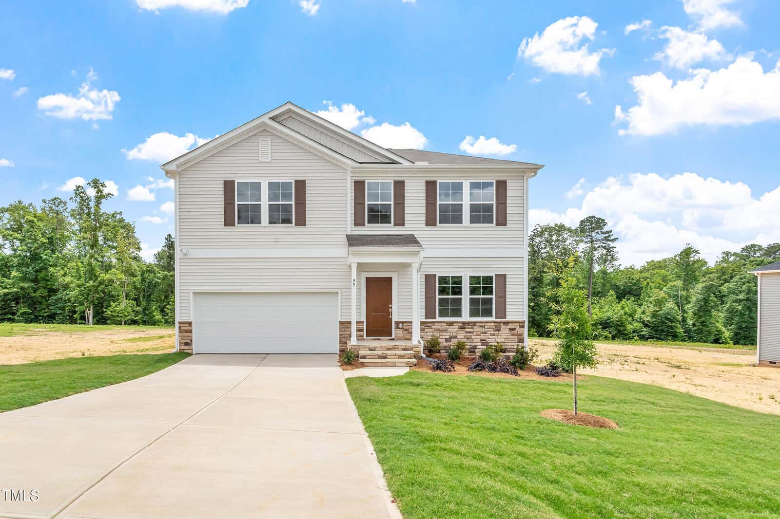A two-story suburban house with white siding, brown shutters, a stone accent, attached two-car garage, and a front lawn. The sky is bright blue with scattered clouds and trees are visible in the background.