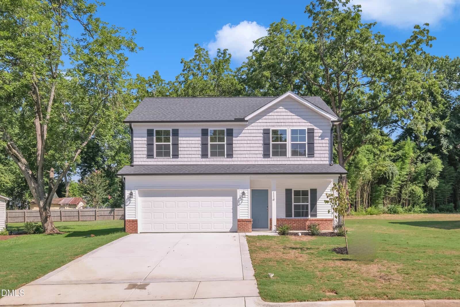 Charming two-story suburban house at 114 Hays Street, Oxford, with light gray siding, dark gray roof, attached two-car garage, and a paved driveway. The yard features green grass, small plants, and is surrounded by tall trees.