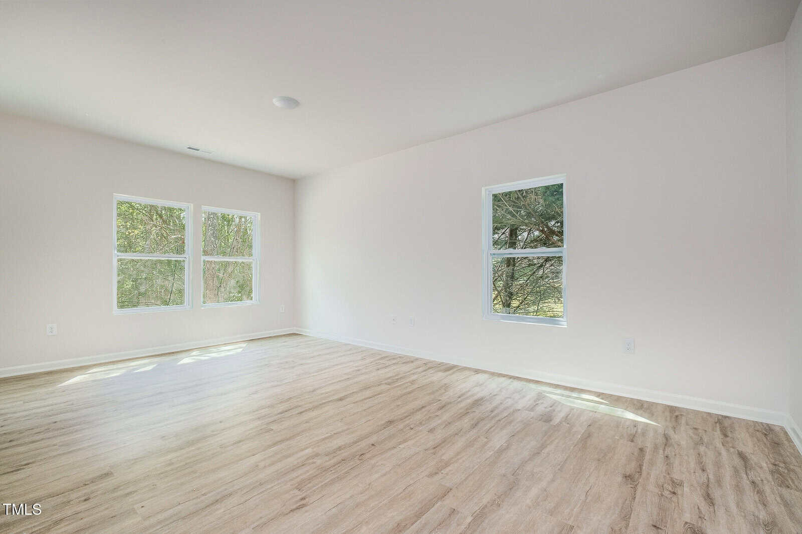 Empty room with light-colored wood flooring, white walls, and three windows letting in natural light. No furniture or decorations are present.