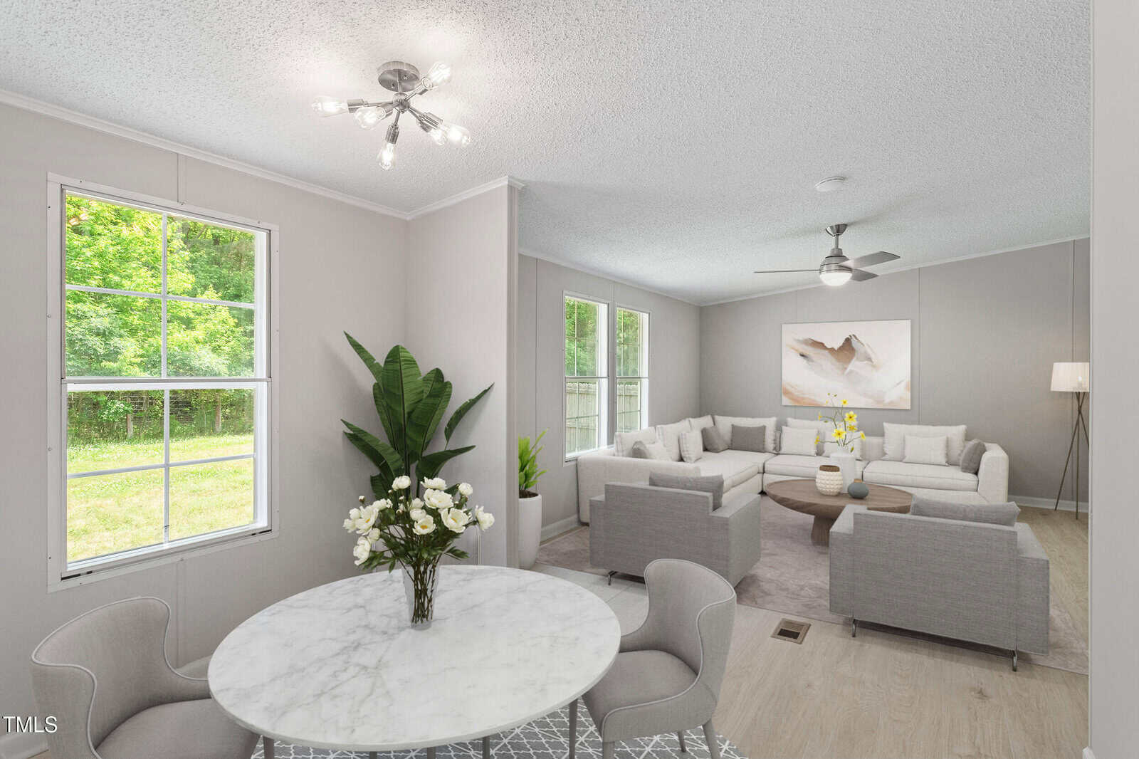 Bright living and dining area with a round marble table, gray chairs, beige sofas, large windows, indoor plants, modern light fixtures, and a neutral-colored painting on the wall.
