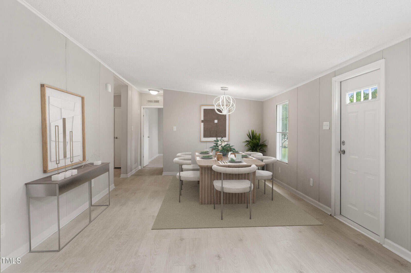 A bright dining room with light wood floors, a modern rectangular table with eight cushioned chairs, a geometric chandelier, minimalist decor, a console table with artwork, and a door and window letting in natural light.