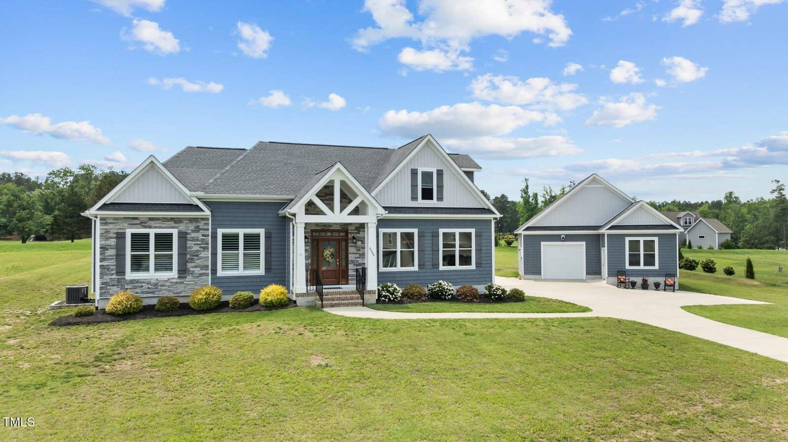 A modern two-story house with gray siding, stone accents, and white trim sits on a large grassy lot at 4564 Ashtons Way in Franklinton. A detached garage is connected by a curved driveway. The sky is partly cloudy.