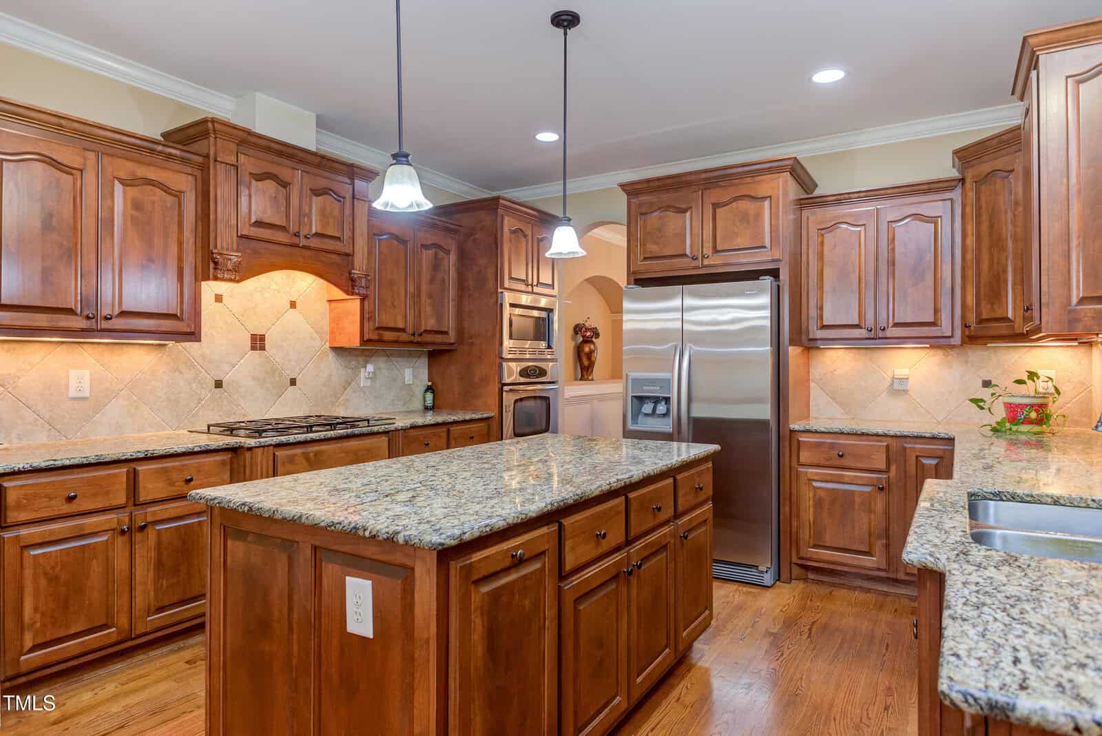 Spacious kitchen with wooden cabinets, granite countertops, a central island, stainless steel appliances, hardwood floors, and pendant lighting above the island.