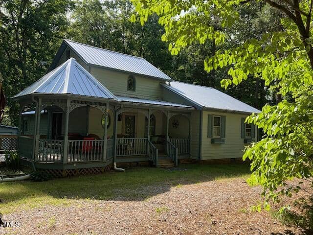 A light green house with a metal roof and a covered front porch sits at 358 Pool Rock Shores Lane, Henderson, surrounded by trees and a gravel driveway on a sunny day.