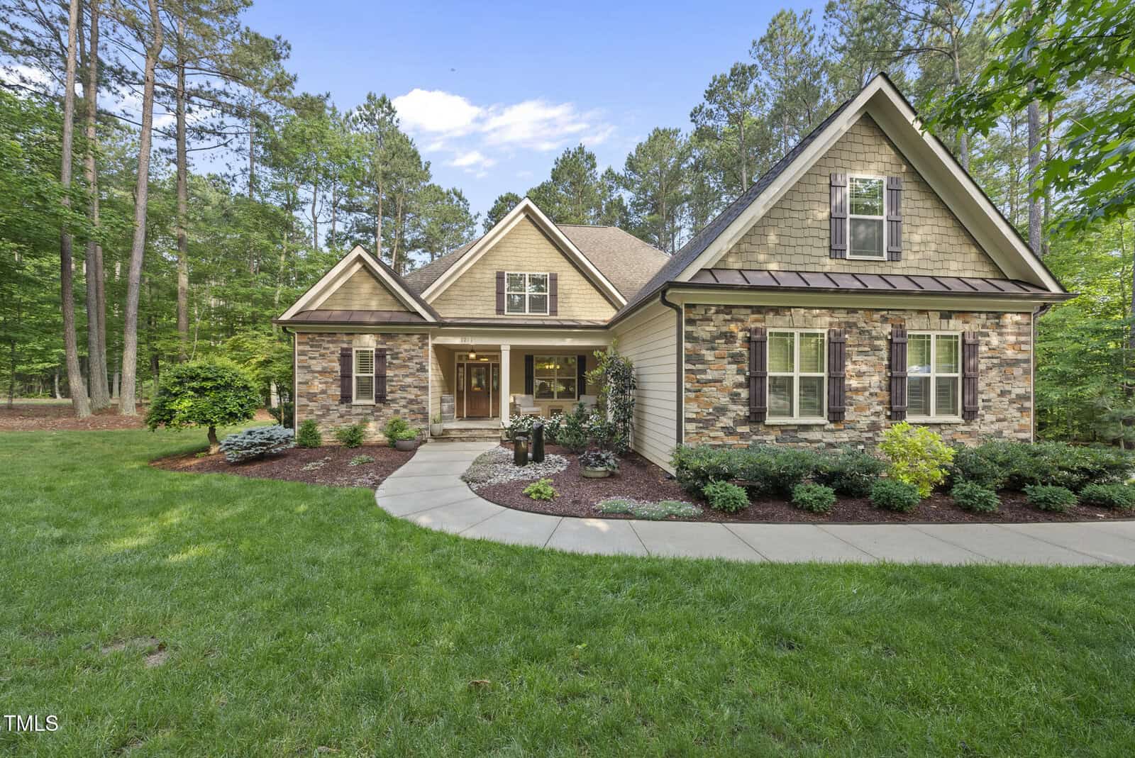 Nestled at 1211 New Grissom Way in Wake Forest, this single-story home features a gable roof, stone and siding exterior, shuttered windows, covered front porch, curved sidewalk, and a beautifully landscaped yard with shrubs and trees.