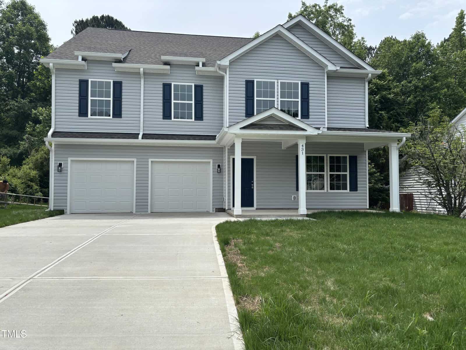 This two-story house at 431 Mayview Drive in Creedmoor features light gray siding, blue shutters, a covered front porch, and a double garage. It sits on a slightly sloped lot with a concrete driveway and patchy green grass out front.