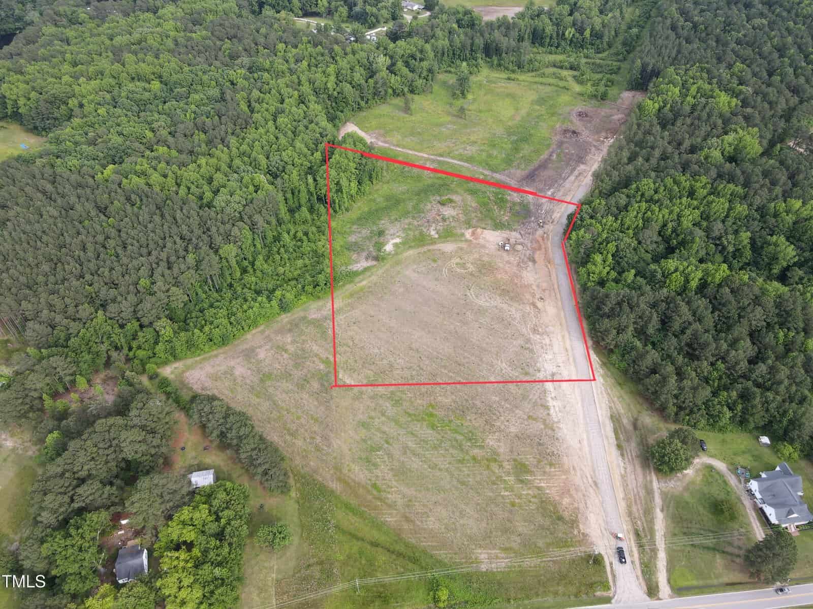 Aerial view of a partially cleared plot of land bordered by trees at 2 Old Hwy 64, Zebulon, with the outlined section marked in red. A gravel road runs along one side, and a few houses are visible nearby.