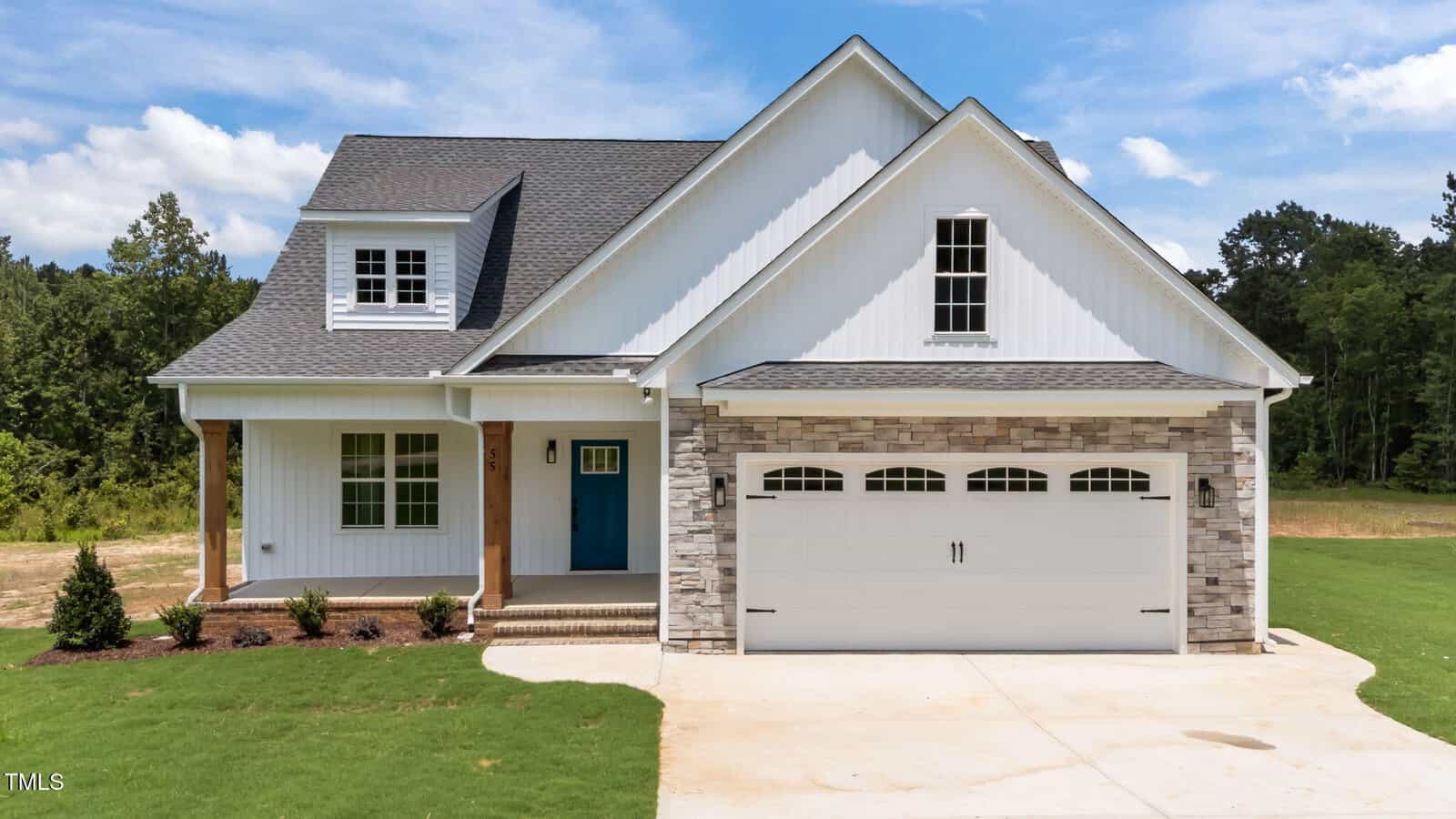 A modern white house with a gabled roof, blue front door, and two-car garage with stone accents sits on a well-kept lawn at 55 Stream View Way, Zebulon, set against a backdrop of trees and blue sky.
