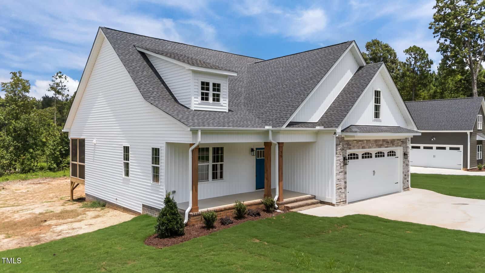 Modern white house with a gray shingle roof, blue front door, stone accents on the garage, and a well-maintained lawn on a sunny day. Trees and another house are visible in the background.