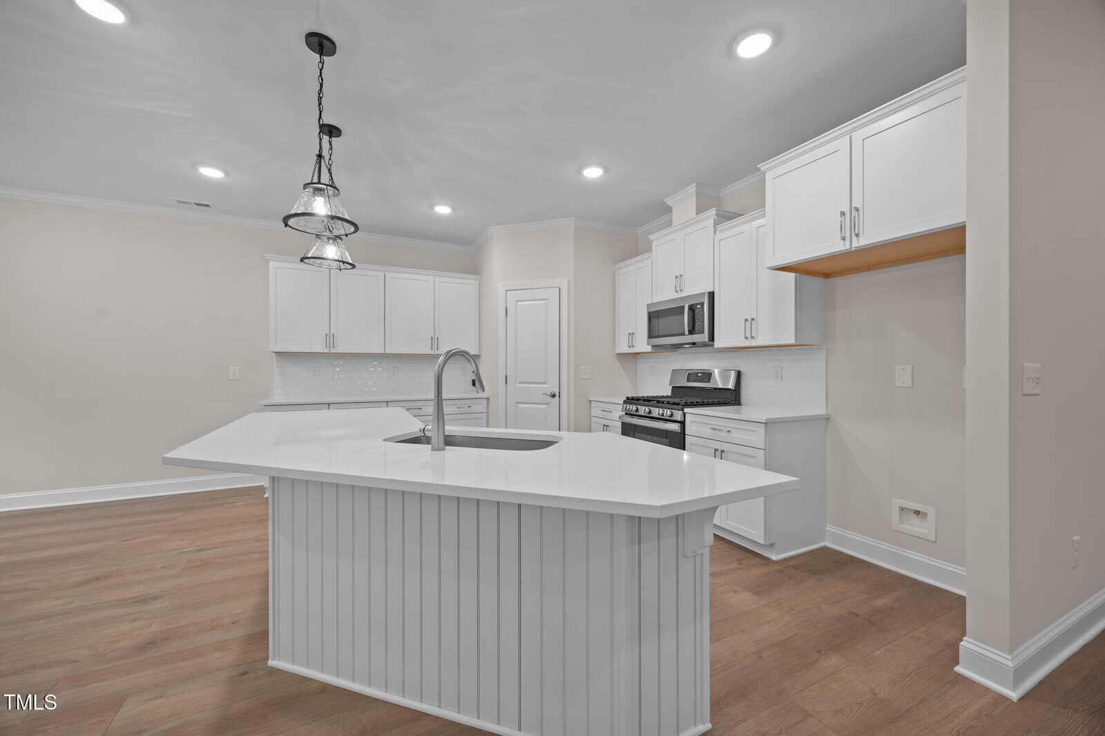 Modern kitchen with white cabinets, stainless steel appliances, a large island with sink, pendant lights, white subway tile backsplash, and light wood flooring.