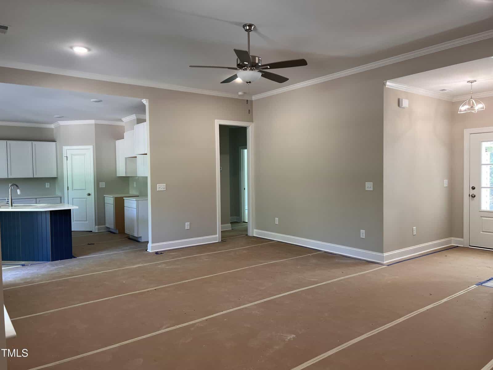 Open-concept living area with beige walls, white trim, ceiling fan, and covered floors. The space includes a kitchen with white cabinets and a dark island, and a back door with glass window panels.