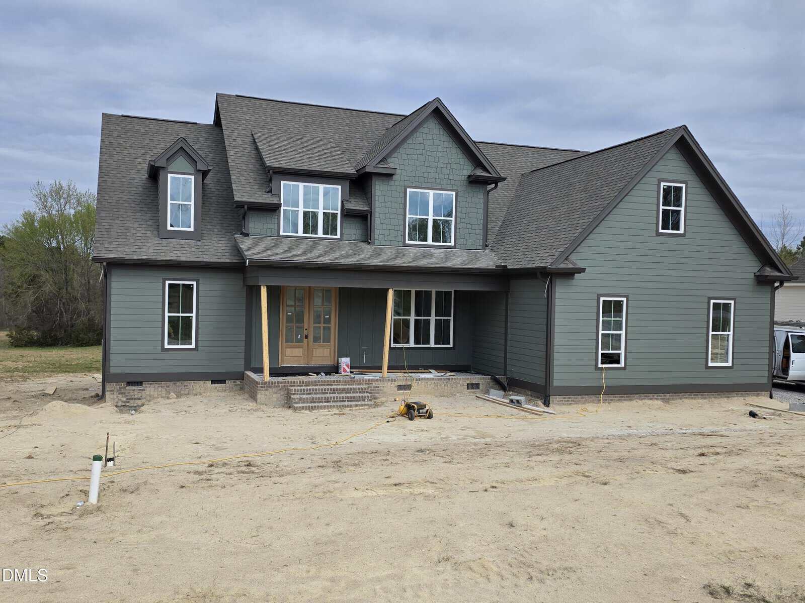 A newly constructed two-story house with green siding, black roof shingles, multiple windows, and unfinished landscaping. Construction materials and tools are visible in the front yard.