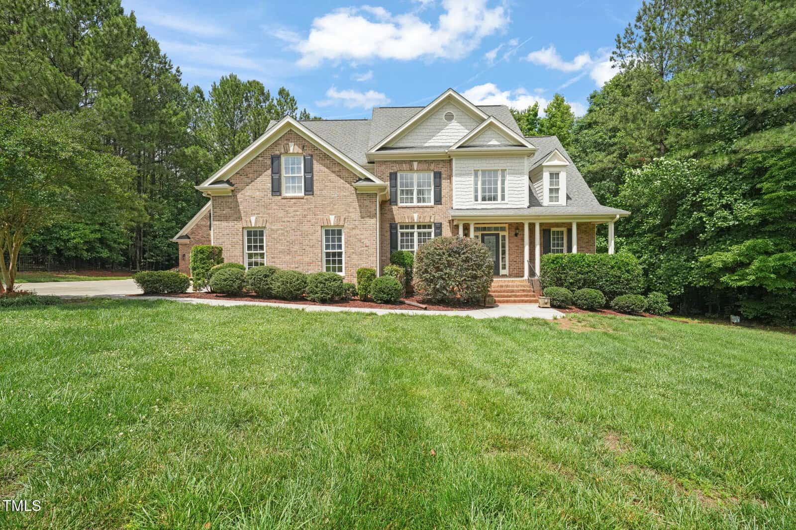 Two-story brick house with white trim, multiple windows, and a covered front porch at 85 Pebble Creek Drive in Franklinton. The house is surrounded by green grass, shrubs, and tall trees under a partly cloudy sky.