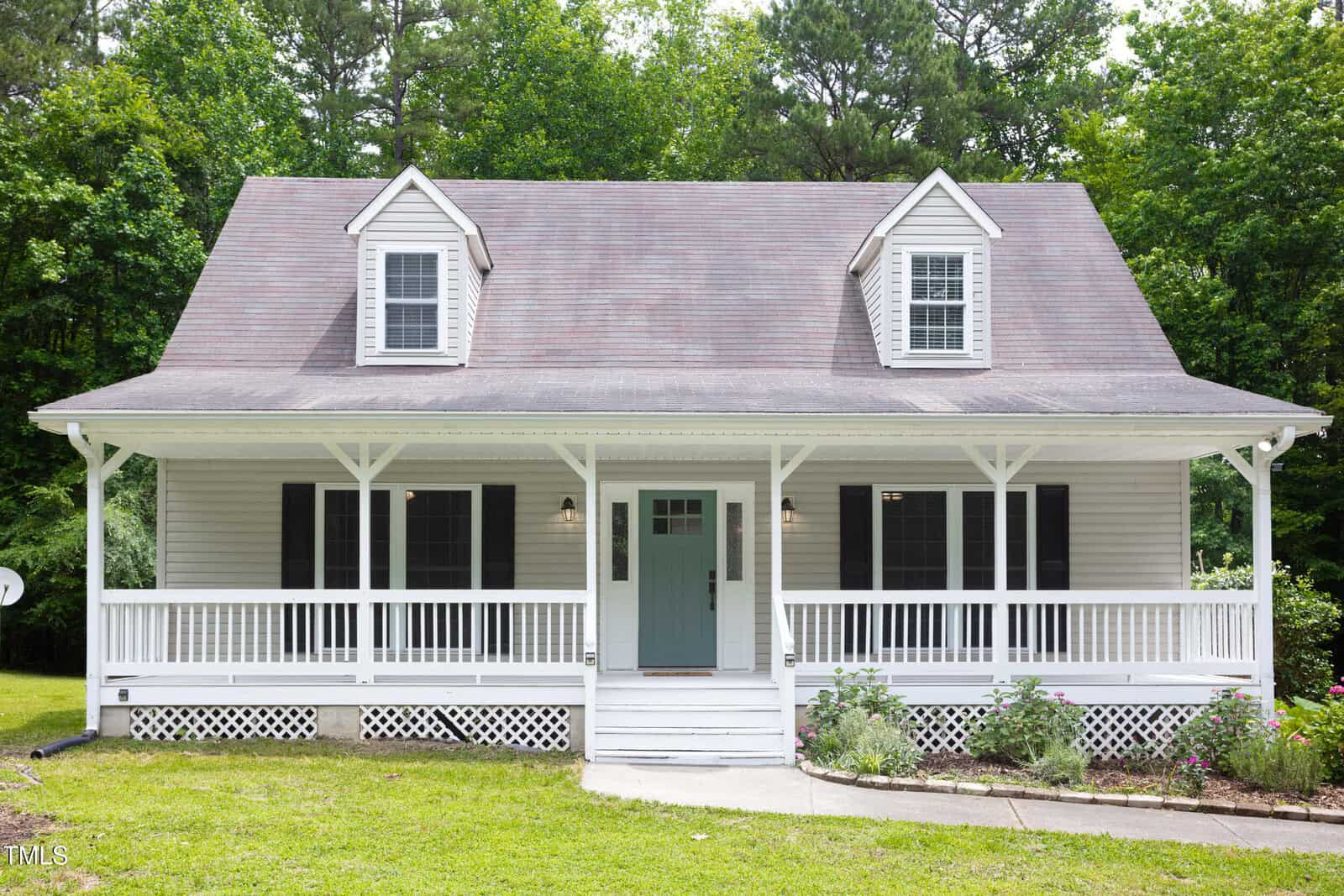 A light gray house at 657 Lakeview Drive in Stem features a covered front porch, two dormer windows, white railings, and a green front door, surrounded by grass and trees in the background.