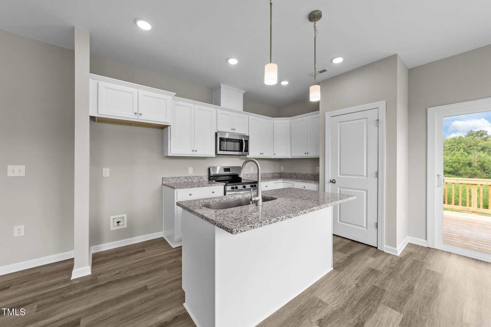 Modern kitchen with white cabinets, granite countertops, stainless steel appliances, a center island with a sink, wood-look flooring, and a door leading to a wooden deck with a view of greenery.