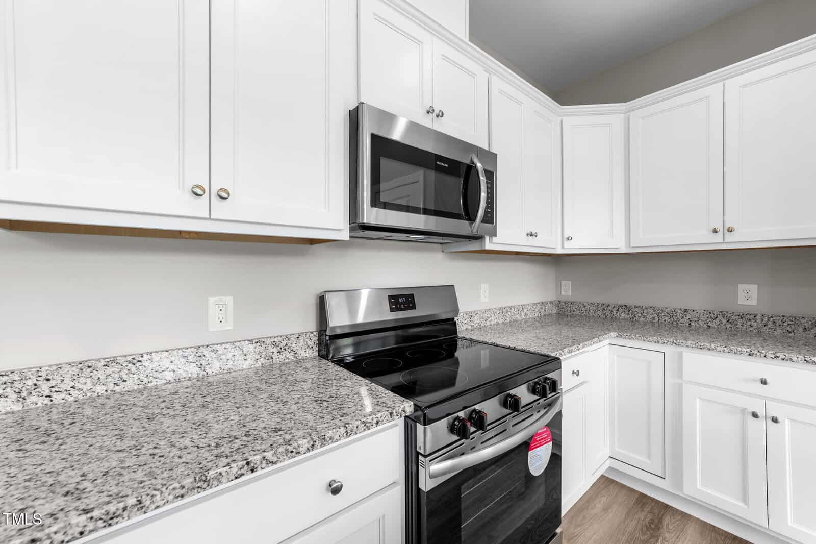 Modern kitchen with white cabinets, granite countertops, a stainless steel electric stove with a black cooktop, and a microwave oven installed above the stove. The cabinets have silver knobs and the walls are painted light beige.