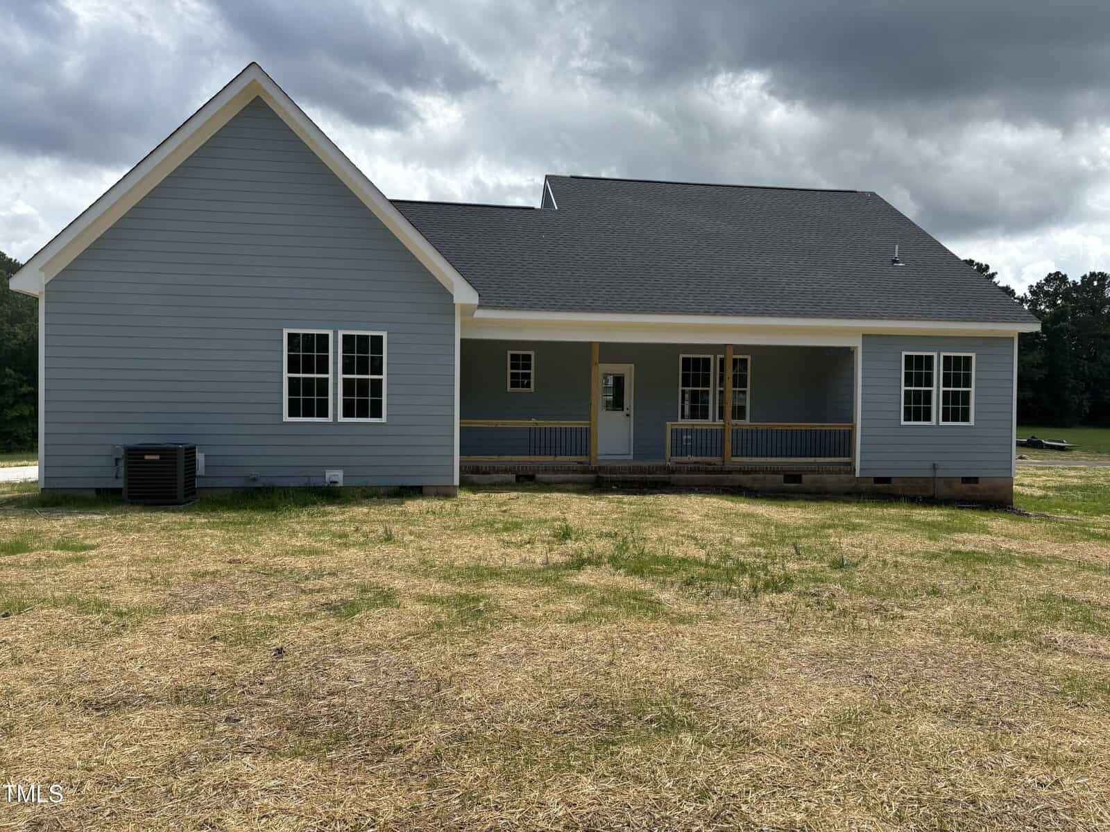 A newly constructed, single-story blue house with white trim, a covered porch, and several windows. The yard is bare with straw covering the ground. The sky is overcast.