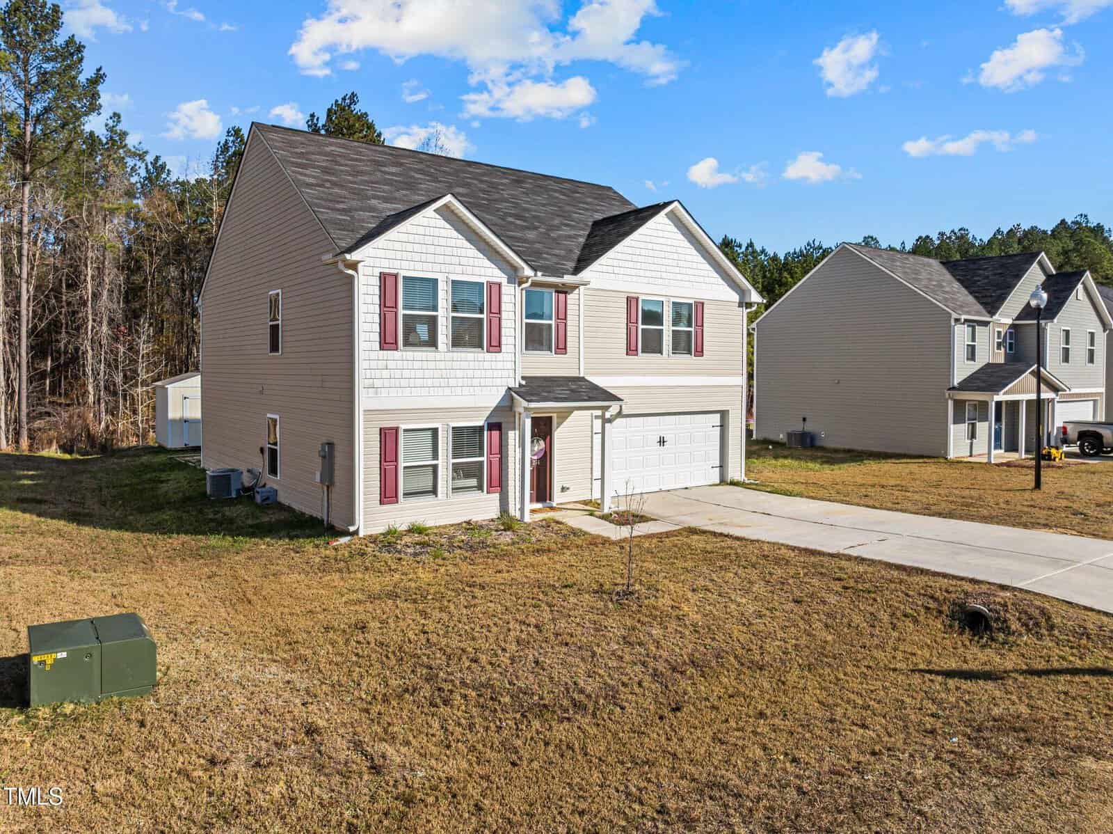 Two-story beige house with red shutters and a double garage at 274 E Boulder Road, Henderson, sits on a large lawn with minimal landscaping. A neighboring house and wooded area are visible in the background under a blue sky.