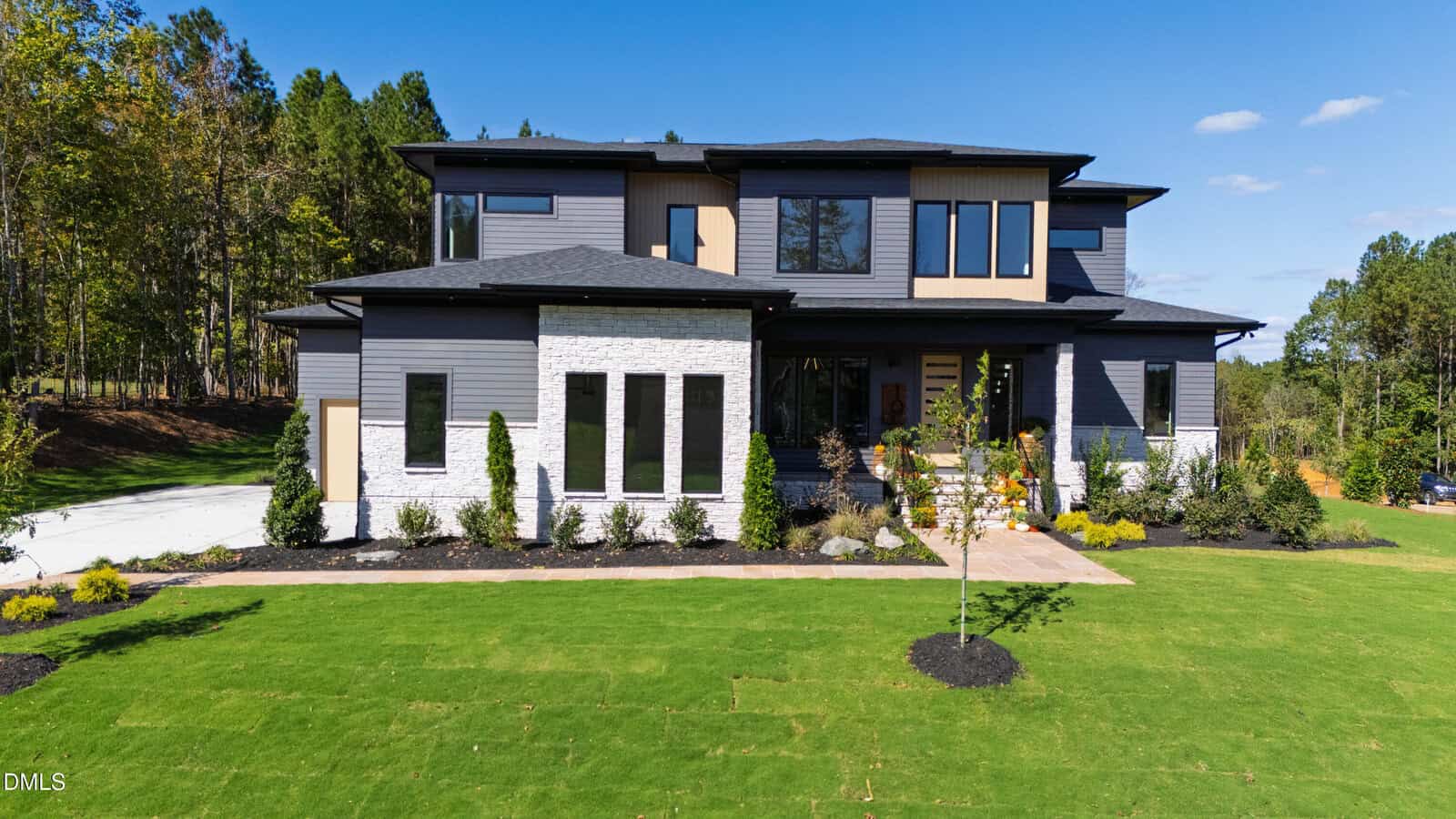A modern two-story house with gray siding, large windows, a covered front porch, and a landscaped yard awaits at 10 Gambel Drive in Youngsville. A driveway is visible to the left, and trees line the background under a clear blue sky.