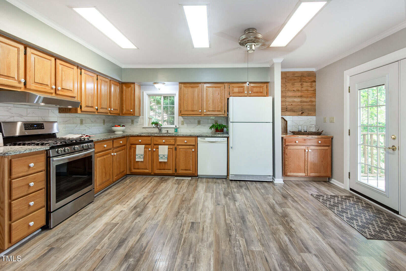 Kitchen with wood cabinets, stainless steel stove, white refrigerator, dishwasher, and microwave. There is a small laundry area, wood and marble accents, vinyl plank flooring, and a door leading to an outside deck.