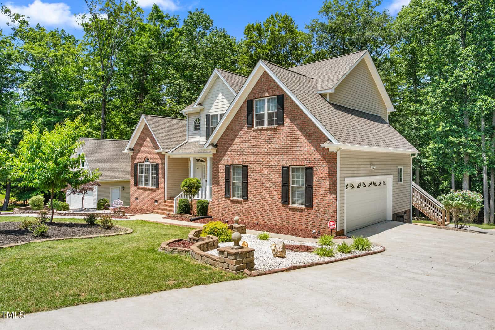 Charming two-story suburban house at 1084 Wild Briar Lane with red brick and light siding exterior, gable roof, attached garage, manicured lawn, landscaped front yard, and tall trees under a clear Stem sky.