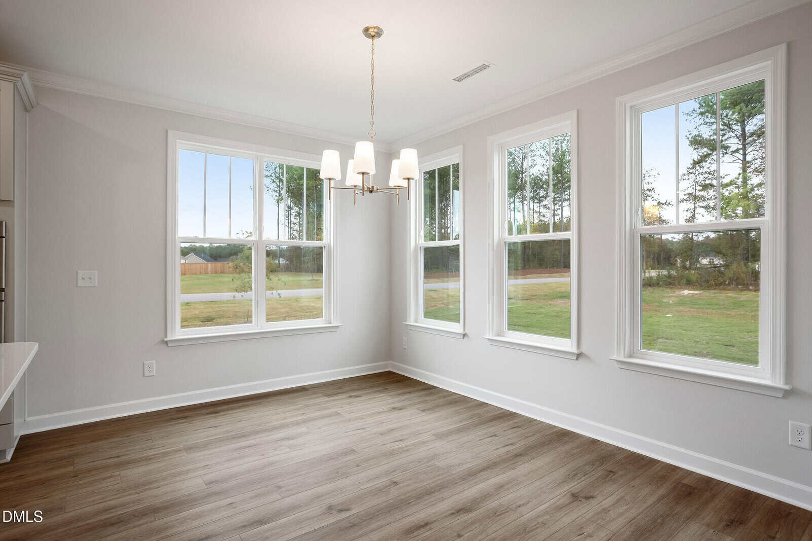 Bright, empty dining area with light wood floors, white walls, large windows offering outdoor views, and a modern chandelier hanging from the ceiling.